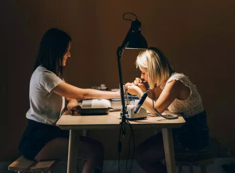 Foto de um procedimento de manicure, manicure atendendo a cliente em sua mesa de trabalho.