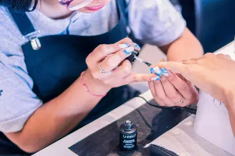 Foto de uma manicure trabalhando, pintando as unhas da cliente.